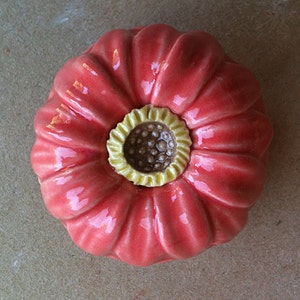 May include: A ceramic flower with a pink glaze and a yellow center. The flower has a textured surface and a rounded shape.