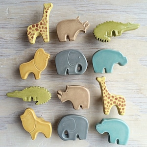 Può includere: Dodici tiretti per cassetti in ceramica a forma di animali di vari colori e design, tra cui una giraffa, un rinoceronte, un coccodrilo, un elefante, un ippopotamo e un leone.