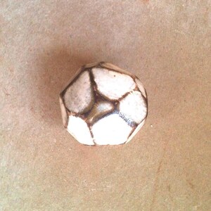 May include: A white ceramic geometric knob with brown accents. The knob has a faceted design and is shaped like a ball.