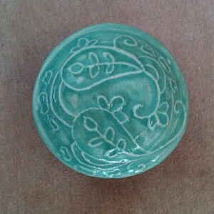 Peut inclure: Un bol en céramique turquoise avec un motif paisley blanc. Le bol est verni et a une finition lisse.