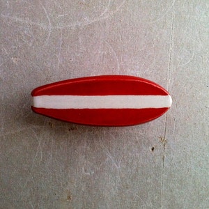 May include: A red and white surfboard-shaped object with a white stripe across the middle.