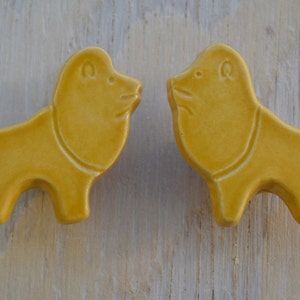May include: Two ceramic lion figurines, facing each other. The lions are a pale yellow color and have a simple, stylized design.