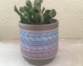 Könnte beinhalten: Eine kleine Sukkulente in einem braunen Keramiktopf mit einem blauen und violetten Ombre-Geometrie-Muster.