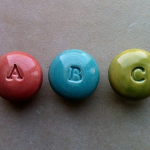 May include: Three round ceramic knobs with the letters A, B, and C in white on a red, blue, and green background.
