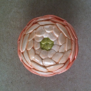 May include: A ceramic flower with a peach-coloured outer layer and a white inner layer. The centre of the flower is a green, five-petal design.