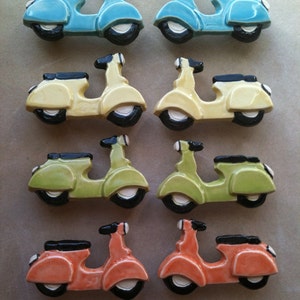 Può includere: Set di otto figurine di scooter in ceramica di vari colori, tra cui blu, giallo, verde e arancione. Ogni scooter ha una sella nera e ruote nere.