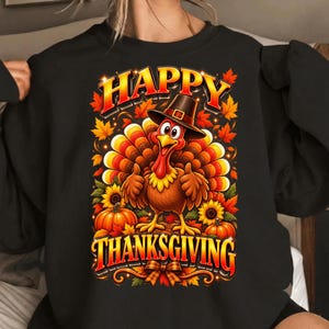 May include: A black sweatshirt featuring a graphic of a turkey wearing a pilgrim hat, giving a thumbs up. The design includes orange and yellow autumn leaves, sunflowers, and pumpkins, with the text HAPPY THANKSGIVING in bold orange letters.