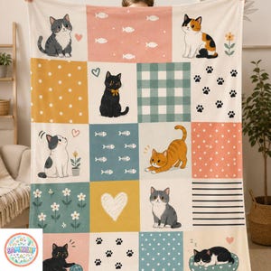 May include: A patchwork blanket featuring various cat illustrations in a grid pattern. The squares include images of cats, hearts, fish bones, paw prints, and polka dots in shades of gray, orange, black, and white. The blanket is held up by a person.