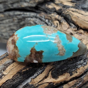 Pu&ograve; includere: Un cabochon di turchese a forma di lacrima con matrice marrone e una tonalit&agrave; blu-verde. La pietra &egrave; posta su un pezzo di legno invecchiato.