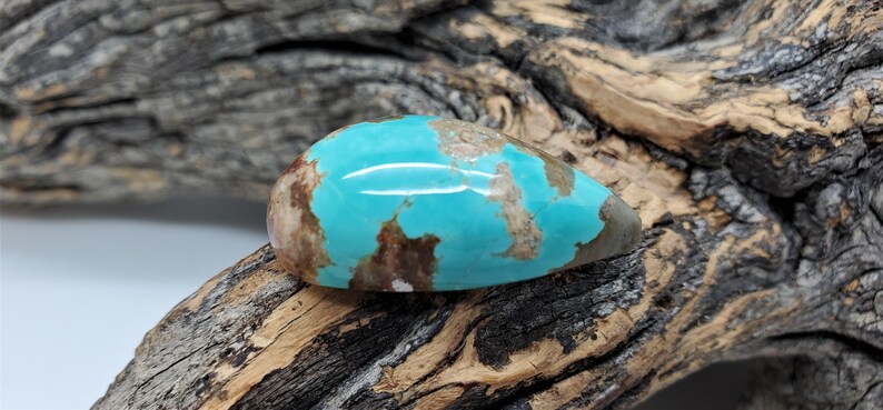 Pu&ograve; includere: Un cabochon di turchese a forma di lacrima con matrice marrone e una tonalit&agrave; blu-verde. La pietra &egrave; posta su un pezzo di legno invecchiato.
