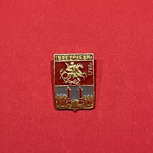May include: A rectangular pin with a red, blue, and gold design. The pin features a knight on horseback, the word "BEPEЯ" in gold lettering, and the year "1782". The pin is set against a red background.