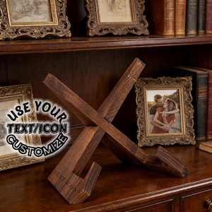 May include: A dark brown wooden book stand with an X-shaped design. The stand has a textured finish and is angled to hold a book. The text "TEXT/ICON" is visible on the stand. The text "USE YOUR TEXT/ICON CUSTOMIZE" is also visible.
