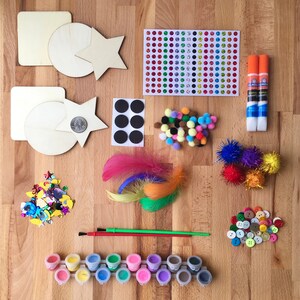 Op de afbeelding: Een knutselset met houten vormen, verf, pompoenen, veren, glitters en lijm. De set bevat ook een vel met kleurrijke stickers en een set magnetische cirkels.