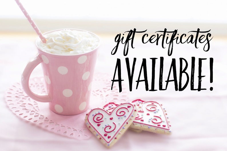 Op de afbeelding: Een roze mok met witte stippen, slagroom en een rietje, twee hartvormige koekjes met roze en witte glazuur en de tekst "gift certificates AVAILABLE!" op een roze achtergrond.