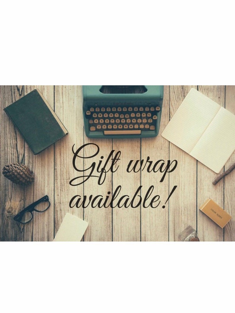 Op de afbeelding: Een vintage typemachine met een groene behuizing en een zwart toetsenbord staat op een houten oppervlak met een boek, een notitieboek, een dennenappel, een bril en een klein doosje. De tekst "Gift wrap available!" is in zwarte cursieve letters op het hout geschreven.