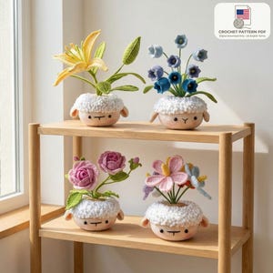 Könnte beinhalten: Vier gehäkelte Blumenarrangements in schafsförmigen Töpfen auf einem Holzregal. Die Blumen sind gelb, blau, rosa und mehrfarbig. Die Töpfe haben eine weiße, flauschige Textur und ein lächelndes Gesicht. Das Regal ist aus hellem Holz.