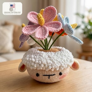 以下が含まれることがあります： カラフルなかぎ針編みの花が入った、羊の形をしたかぎ針編みの植木鉢。 植木鉢はクリーム色で、ふわふわの白い上部、ピンクの頬、笑顔の顔が付いています。 花はピンク、黄色、オレンジ、青です。