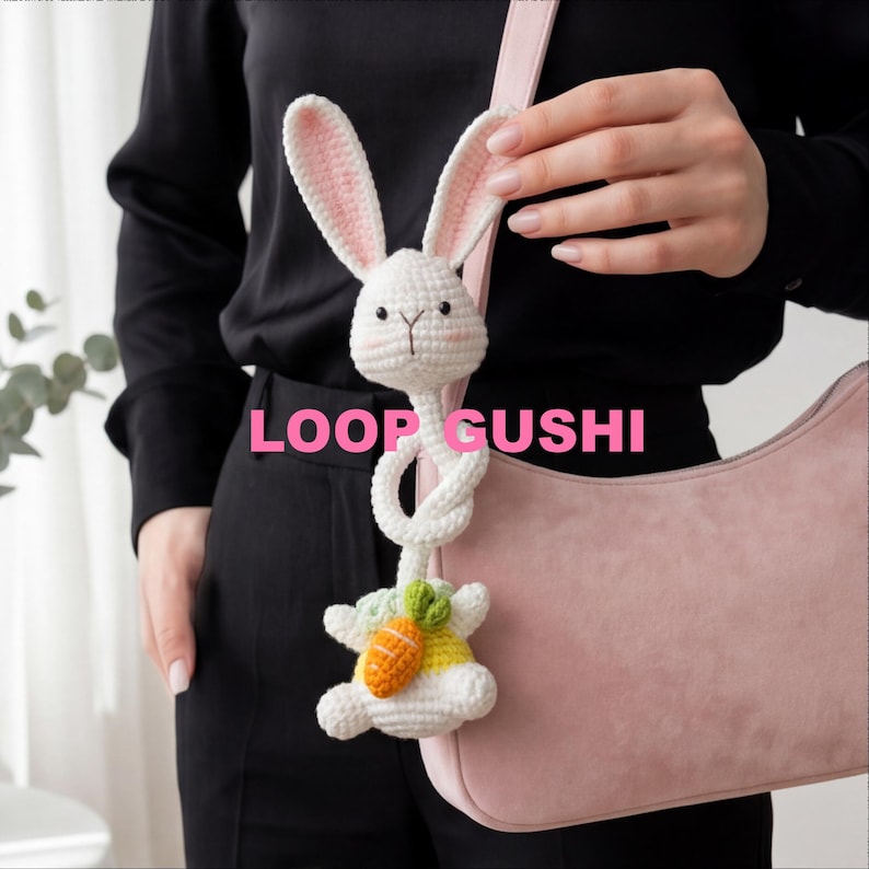 Pu&ograve; includere: Un ciondolo a forma di coniglietto bianco all'uncinetto con interno orecchie rosa e una carota. Il coniglietto &egrave; attaccato a una borsa rosa. Il testo "LOOP GUSHI" &egrave; visualizzato in rosa.