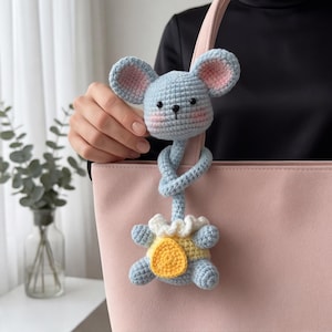 Pu&ograve; includere: Un giocattolo a forma di topo all'uncinetto blu chiaro con orecchie interne rosa e un completo giallo e bianco. Il topo &egrave; attaccato a un manico di borsa rosa chiaro. Il giocattolo &egrave; fatto a mano e ha un design stravagante.