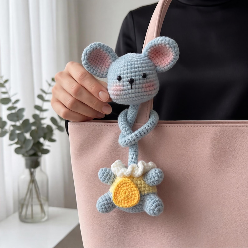 Pu&ograve; includere: Un giocattolo a forma di topo all'uncinetto blu chiaro con orecchie interne rosa e un completo giallo e bianco. Il topo &egrave; attaccato a un manico di borsa rosa chiaro. Il giocattolo &egrave; fatto a mano e ha un design stravagante.