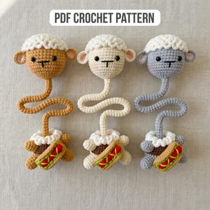 Pu&ograve; includere: Tre pecorelle all'uncinetto in beige, bianco e grigio, ciascuna con un lungo collo curvo e una base a forma di hot dog. Le pecore hanno soffice lana bianca, piccole orecchie e occhi neri. Il testo "PDF CROCHET PATTERN" &egrave; in alto.