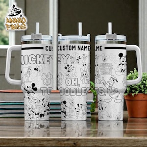 A set of three personalized tumblers featuring the characters from the Disney movie " Mickey Mouse". The tumblers have a black and white design with various Disney characters and phrases, such as " Mickey Mouse", "OH, TOODLES", and "Mishka". The tumblers are placed on a wooden surface, with a potted plant visible in the background.