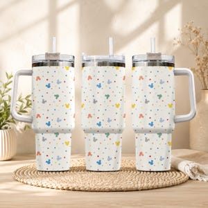 Pode incluir: Tr&ecirc;s copos brancos com al&ccedil;as e tampas transparentes com canudos. Os copos apresentam um padr&atilde;o repetitivo de pequenas silhuetas coloridas da cabe&ccedil;a do Mickey Mouse e pontos s&oacute;lidos em tons de laranja, azul, amarelo, verde e cinza sobre fundo branco.