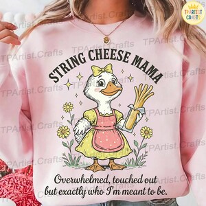 Könnte beinhalten: Hellrosa Sweatshirt mit einer Grafik einer Cartoon-Ente in einem gelben Kleid und einer rosa Schürze, die Käsefäden hält. Der Text "STRING CHEESE MAMA" wölbt sich über der Ente, mit dem Satz "Overwhelmed, touched out but exactly who I'm meant to be" darunter.