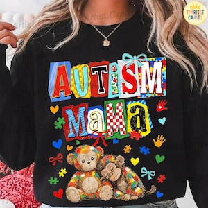 May include: Black sweatshirt with the words "AUTISM MAMA" in colorful block letters. The design includes puzzle pieces, hearts, handprints, and two stuffed monkeys. The monkeys are in a rainbow of colors.