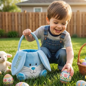 May include: A young child smiles while holding a light blue Easter basket shaped like a bunny. The basket has the name "James" embroidered on it. Colorful Easter eggs are scattered in the grass, and a small lamb plush toy is visible.