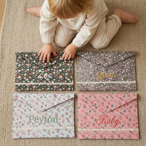 May include: Four floral print document holders with personalized names: Zoe, Grace, Peyton, and Ruby. Each holder features a different floral pattern in shades of green, gray, blue, and pink, with a white lace trim. The names are embroidered in complementary colors.