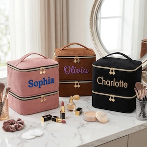 May include: Three corduroy makeup bags in pink, brown, and black, each with a name embroidered on the front: Sophia, Olivia, and Charlotte. The bags have gold zippers and handles. Makeup and accessories are arranged on a marble surface.