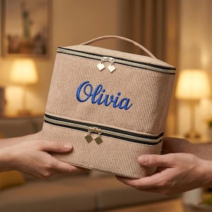 Può includere: Un beauty case in velluto a coste beige con manico e due scomparti con cerniera. Il nome "Olivia" è ricamato in blu sul davanti. La borsa ha tiretti dorati e un bordo con cerniera nero.