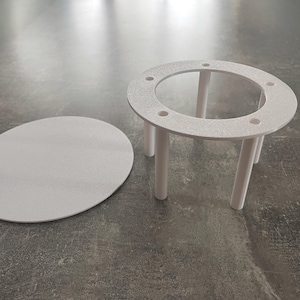 Puede incluir: Una mesa blanca circular con cuatro patas y una tapa ovalada a juego. La mesa tiene una superficie texturizada. La tapa de la mesa está separada de la mesa. La mesa está diseñada para un propósito específico.