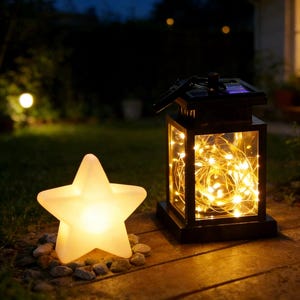 Op de afbeelding: Een gloeiende stervormige lamp en een zwarte lantaarn met warmwitte lichtsnoeren. De lantaarn heeft een zonnepaneel aan de bovenkant. De ster staat op kleine stenen en de lantaarn op een houten oppervlak. De scène speelt zich buiten af in de schemering.