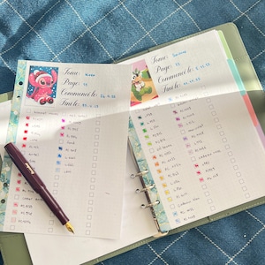 May include: An open planner with handwritten notes and colorful check boxes. A maroon fountain pen rests on the left page. Decorative stickers of cartoon characters are visible. The planner is open on a blue patterned surface.