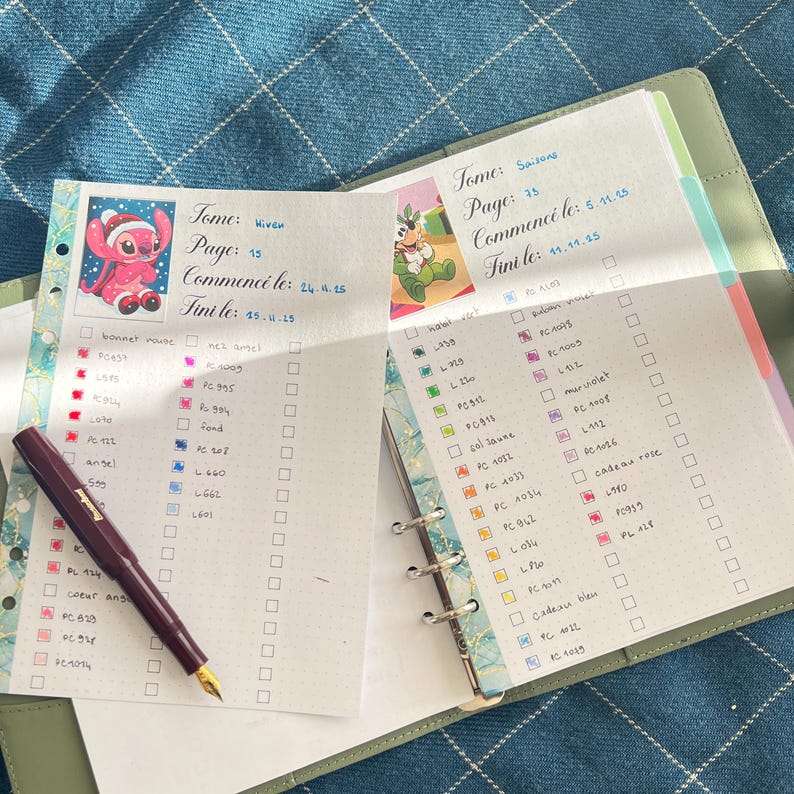 May include: An open planner with handwritten notes and colorful check boxes. A maroon fountain pen rests on the left page. Decorative stickers of cartoon characters are visible. The planner is open on a blue patterned surface.