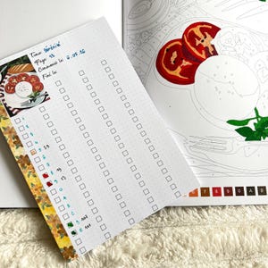 May include: A white dotted paper with a checklist and the text "Tome: B&eacute;r&eacute;nit&eacute;, Page 13, Commenc&eacute; le: 6.05.16, Fini le". A color-by-number book is visible in the background. A decorative floral tape is on the left side.