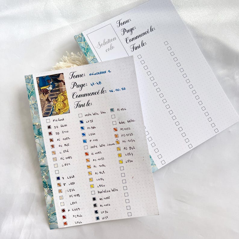 May include: Two open notebooks with a floral border. One page has a colorful illustration and a checklist with color swatches. The other page has a checklist with dotted lines. Text includes "Tome", "Page", "Commenc&eacute; le", and "Fini le".
