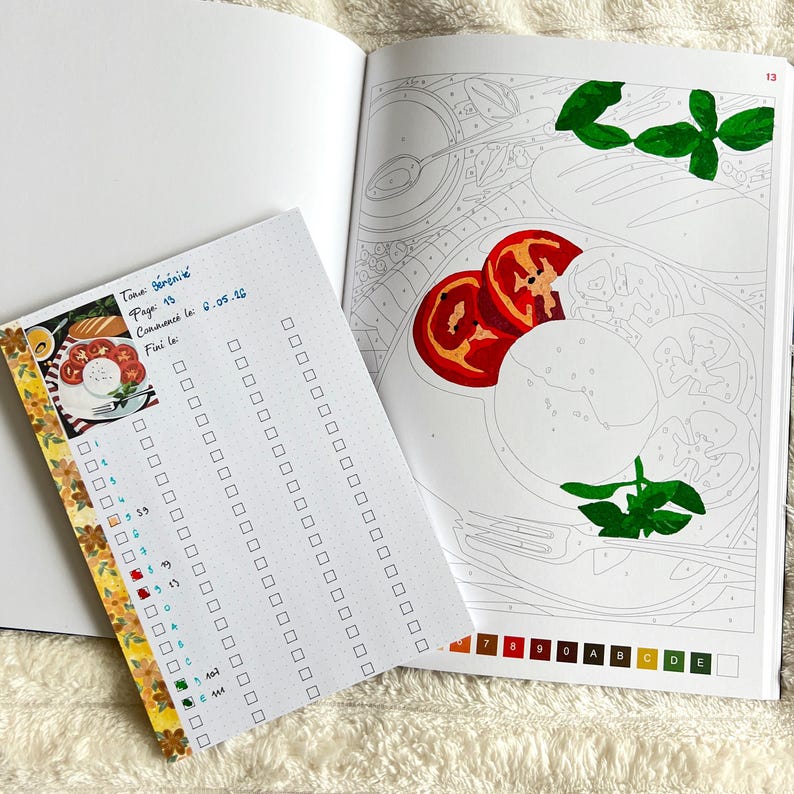 May include: Open coloring book page with a partially colored image of tomatoes, mozzarella, and basil. A small notepad with a checklist and text in French is on the left. The notepad is decorated with floral washi tape.