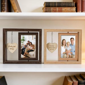 Op de afbeelding: Twee rechthoekige houten fotolijsten met een draaibaar binnenframe. De donkerbruine lijst heeft een hartvormige bedel met de inscriptie "Family first always". De licht eiken lijst heeft een hartvormige bedel met "Family: where love grows."