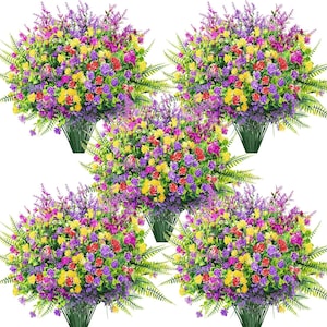 Peut inclure: Cinq bouquets de fleurs artificielles colorées. Chaque bouquet présente un mélange de fleurs violettes, jaunes, rouges et de feuillage vert. Les fleurs sont disposées dans une base verte en forme de pot, créant un affichage vibrant et décoratif.
