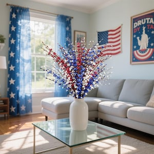 Op de afbeelding: Een witte vaas met rode, witte en blauwe bloemstelen staat op een salontafel met glazen blad. De kamer heeft blauwe sterrengordijnen, een Amerikaanse vlag en een bank, wat een patriottisch thema cre&euml;ert. De vaas is ongeveer 30 cm hoog.