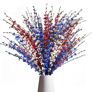 Op de afbeelding: Een boeket kunstbloemen in een witte vaas. De bloemen zijn rood, wit en blauw, wat een patriottisch kleurenschema cre&euml;ert. De bloemen zijn dicht op elkaar geplaatst en hebben een interessante textuur, ideaal voor decoratie.