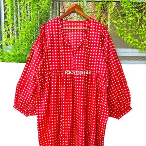 Puede incluir: Un vestido a cuadros rojo y blanco con mangas largas y cuello en V. El vestido tiene un diseño suelto y fluido y está hecho de una tela ligera. El texto "RKS Textile" es visible en el vestido.