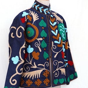 Pode incluir: Uma jaqueta azul marinho com bordados florais coloridos. A jaqueta apresenta uma gola alta e é adornada com padrões bordados de flores e folhas verdes, vermelhas, marrons e azuis. O bordado é detalhado e cobre a frente e as mangas.