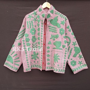 以下が含まれることがあります： ピンクとグリーンの刺繍入りジャケット。ハイカラーと長袖が特徴です。ジャケットは、繰り返しの幾何学模様と、緑色の刺繍の花柄と鳥のデザインが特徴です。「RKS Textile」の文字が前面に表示されています。