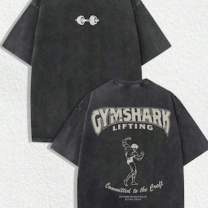 May include: Dark gray t-shirt with a white barbell graphic on the front and a "Gymshark Lifting" design with a weightlifter illustration on the back. The shirt also has the text "Committed to the Craft".