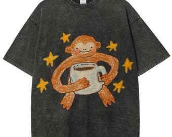 May include: Dark gray t-shirt featuring a cartoon monkey holding a coffee cup, surrounded by yellow stars. The monkey is drawn in shades of brown and orange, with a smiling expression. The shirt has a vintage, washed-out look.