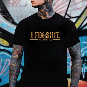 May include: Black t-shirt with the text "I FIX SHIT. THAT'S WHAT I DO" in a gold color. The text is centered on the front of the shirt. The shirt is short-sleeved.